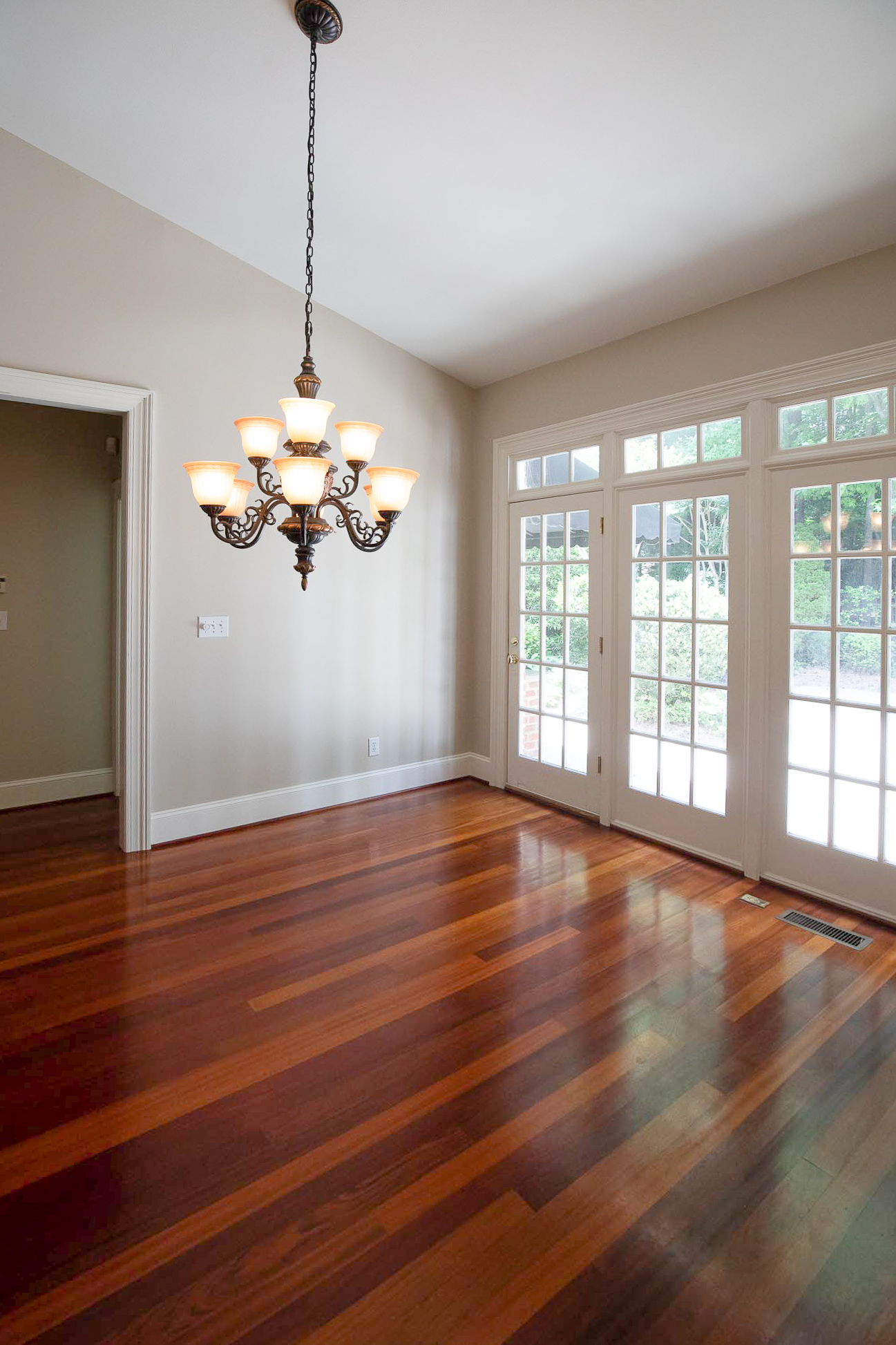 An empty white dining room with cherry red floors and small chandelier