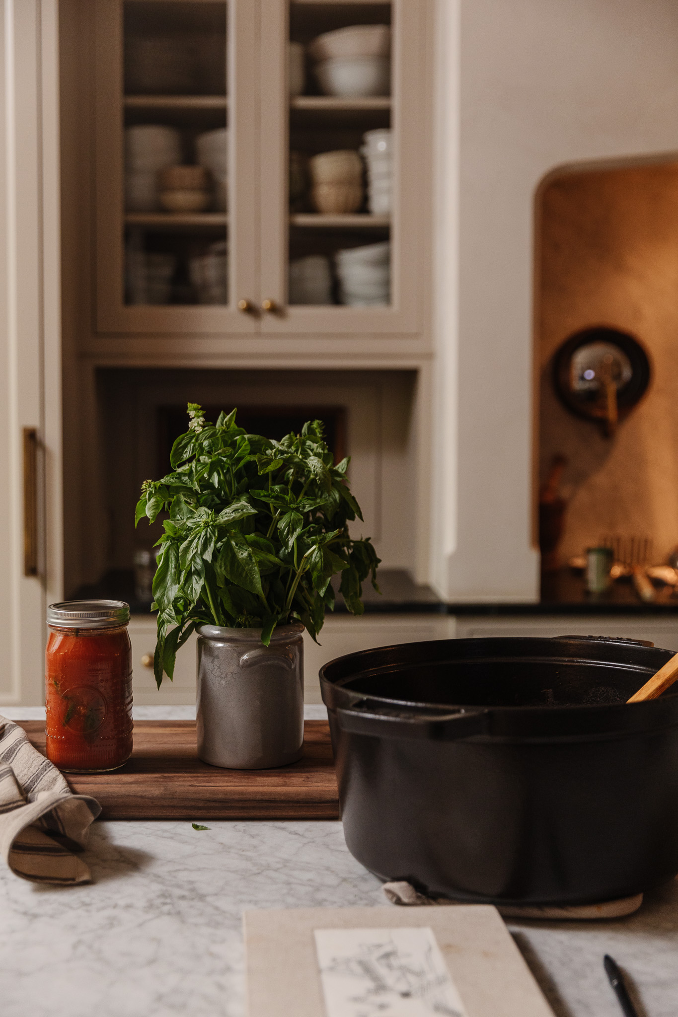 A jar of tomato sauce next to a container of fresh basil and a black stockpot