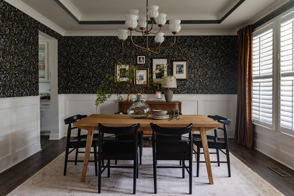 A blue dining room with dark floral wallpaper, black chairs and a vintage-modern chandelier