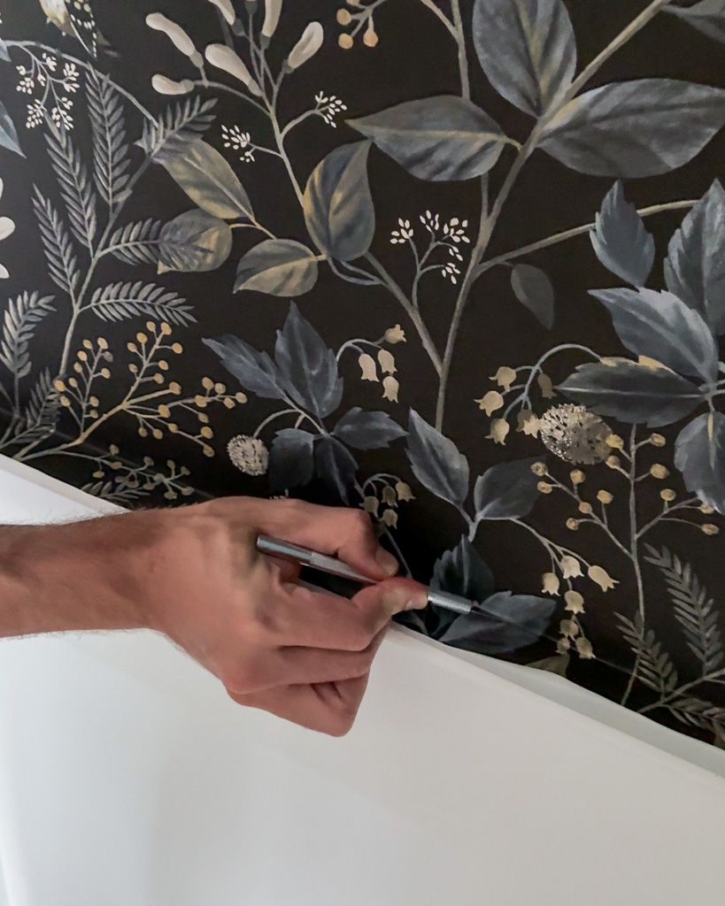 Hand using an X-acto knife to trim an edge of peel-and-stick wallpaper