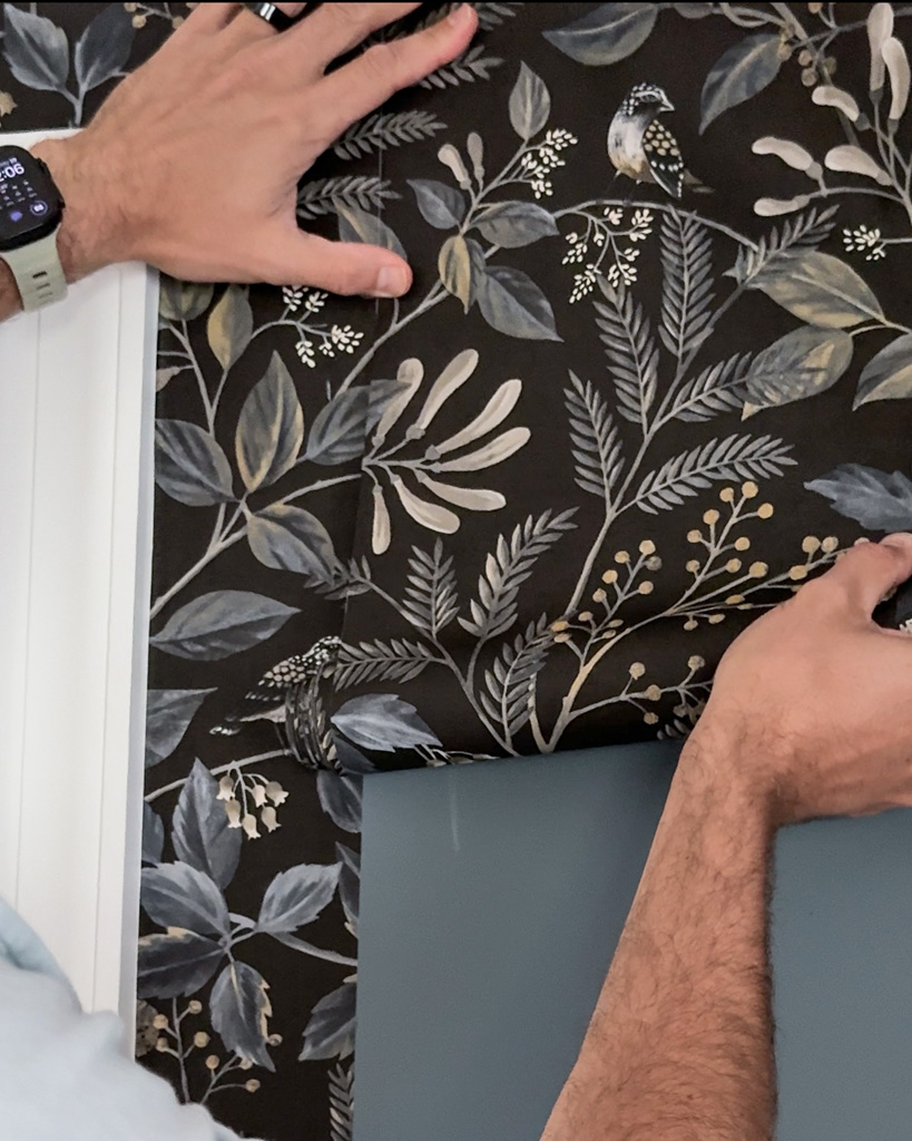 Hands matching the repeat pattern of a dark floral wallpaper