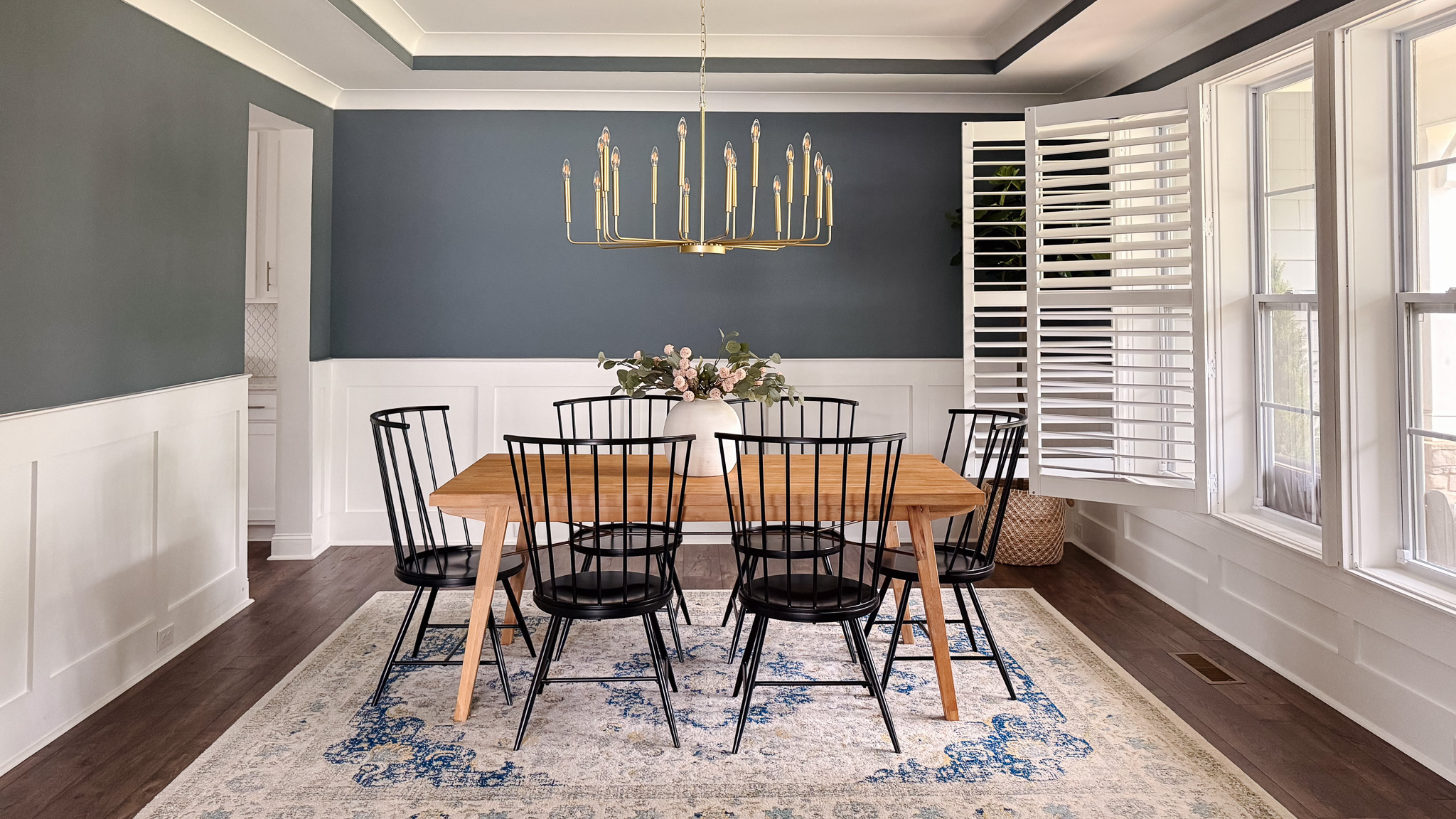 A blue dining room with black spindle chairs and a gold chandelier