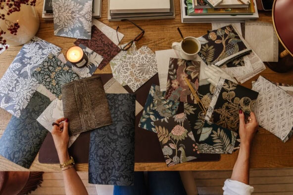 Overhead of someone at a desk reviewing squares of moody traditional wallpaper designs scattered