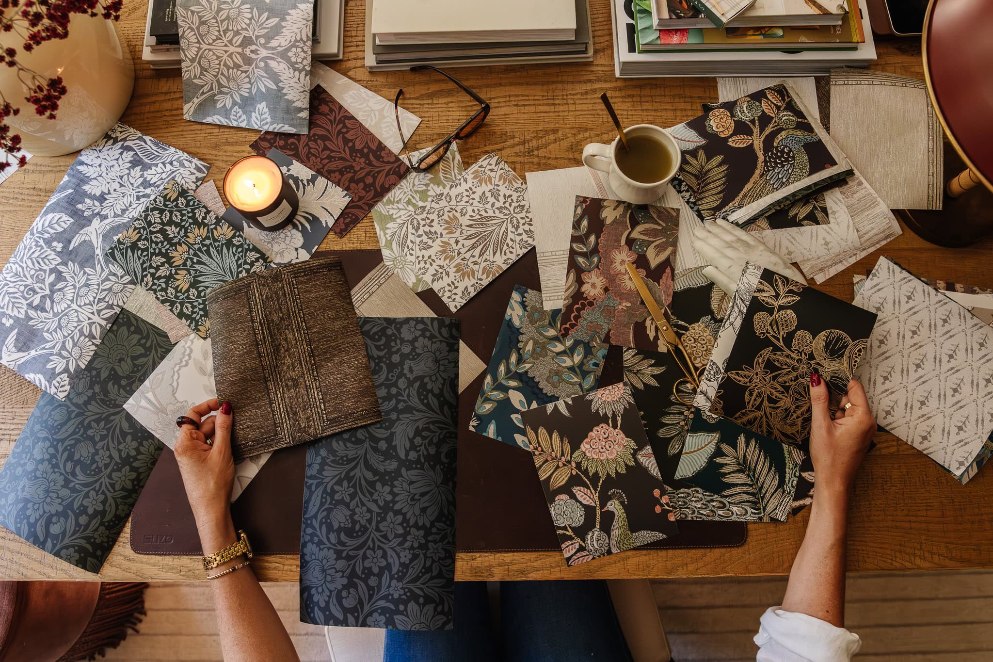 Overhead of someone at a desk reviewing squares of moody traditional wallpaper designs scattered