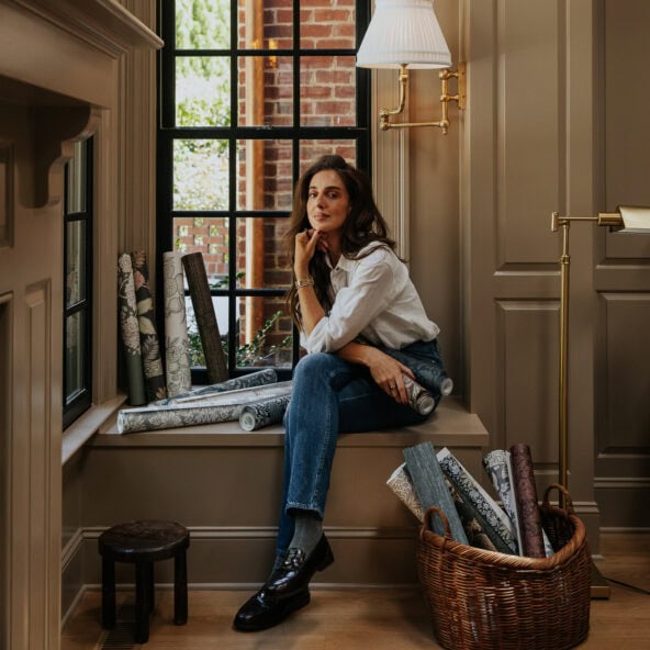 Julia sitting on a windowsill in the living room with rolls of wallpaper in baskets and on the sill beside her