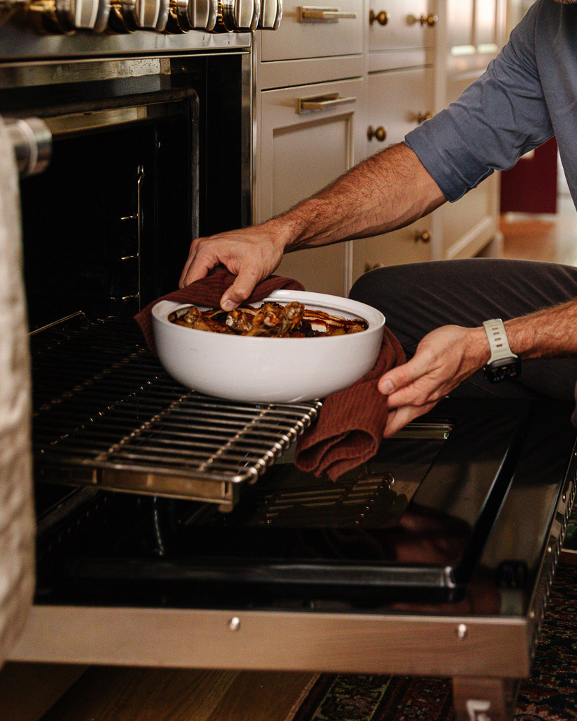 Chris pulling a tagine pot out of the oven filled with braised chicken