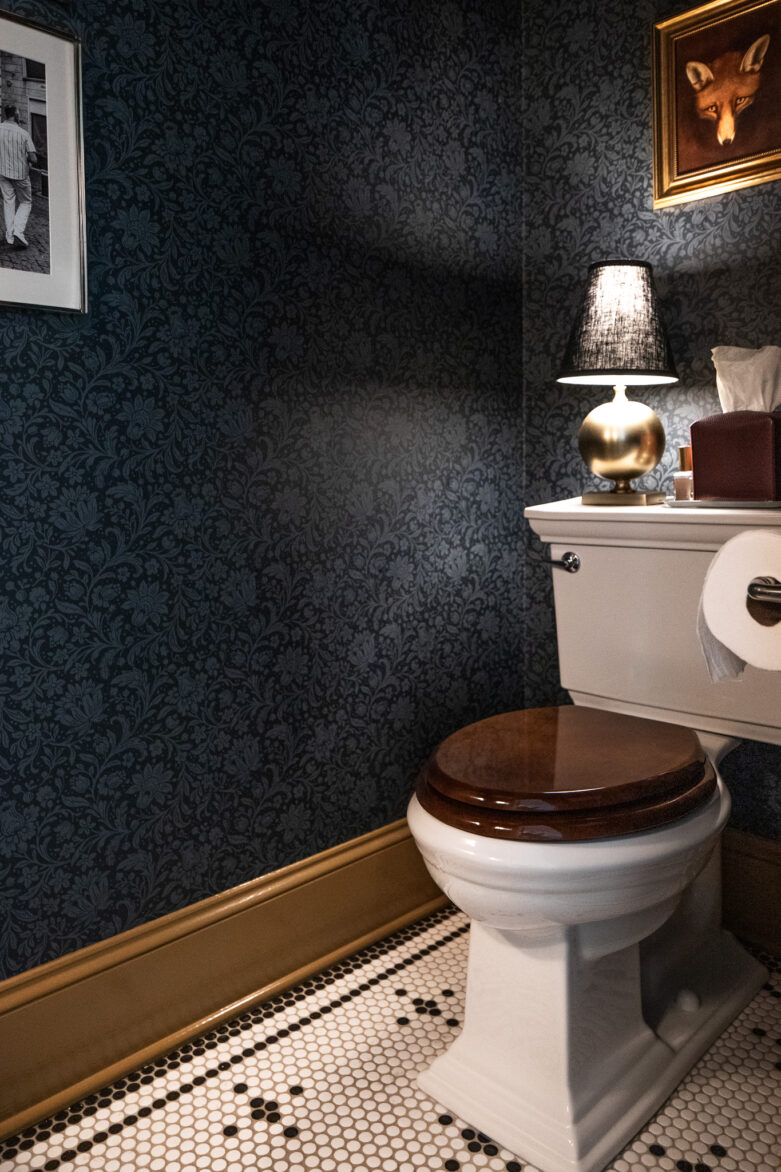 A penny tile floor in a moody traditional bathroom with a wood seat cover on the toilet