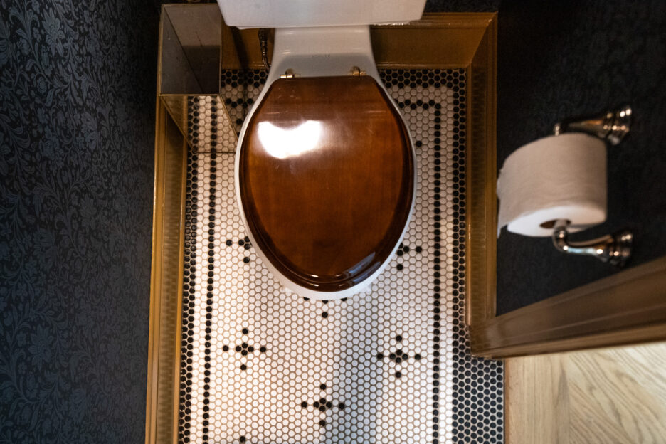 Overhead of the wooden seat cover on the toilet and the penny tile floors