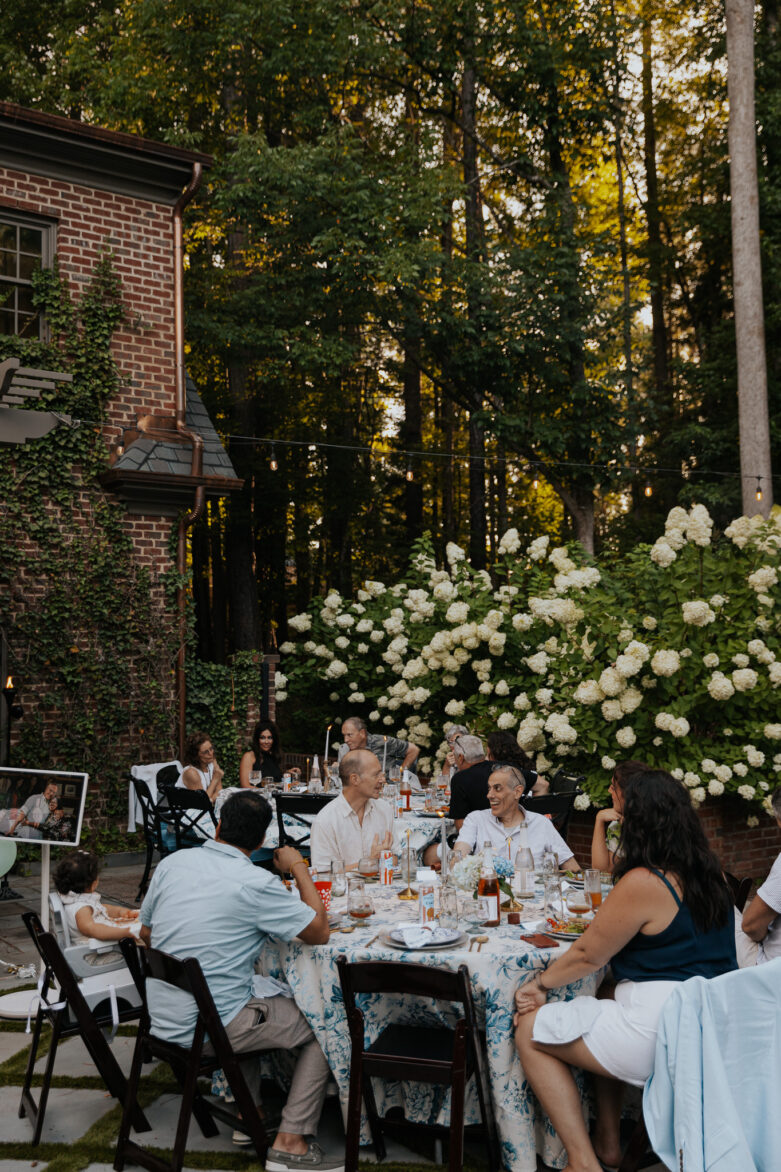 An outdoor dinner party with guests enjoying chatting with each other next to a portable TV with photo memories
