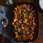 Roasted sweet potatoes with red onions and herbs in a black cast iron skillet on a wooden table, styled for a cozy home dinner, showcasing kitchen and dining room decor.