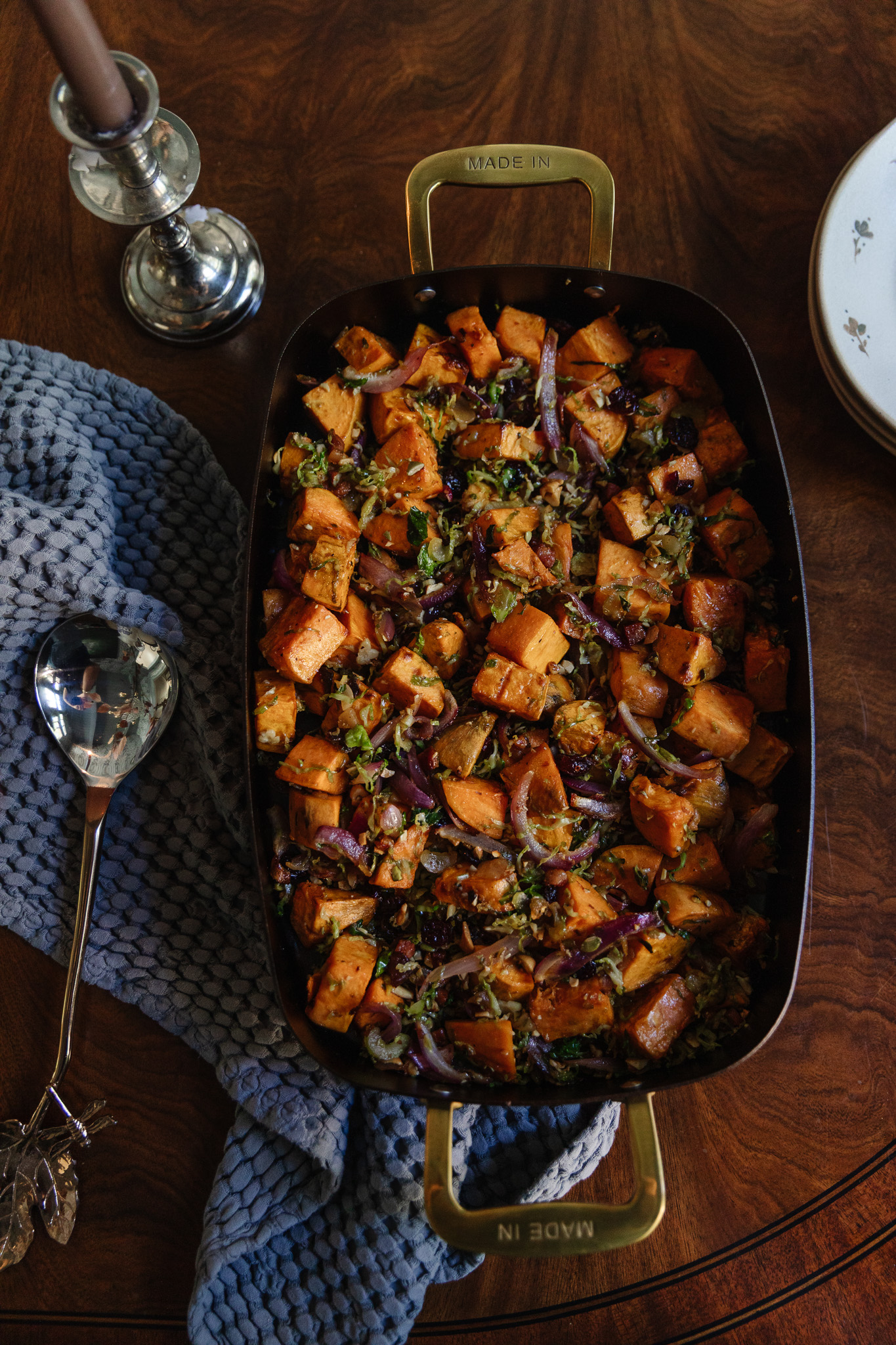 Roasted sweet potatoes with red onions and herbs in a black cast iron skillet on a wooden table, styled for a cozy home dinner, showcasing kitchen and dining room decor.