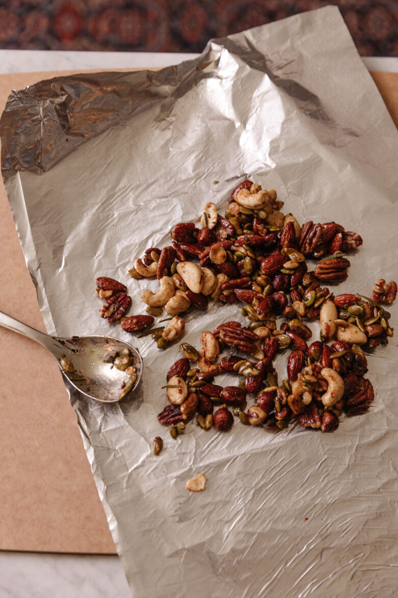 Mixed roasted nuts on parchment paper, including cashews, pecans, and pumpkin seeds, ready for snacking or baking.