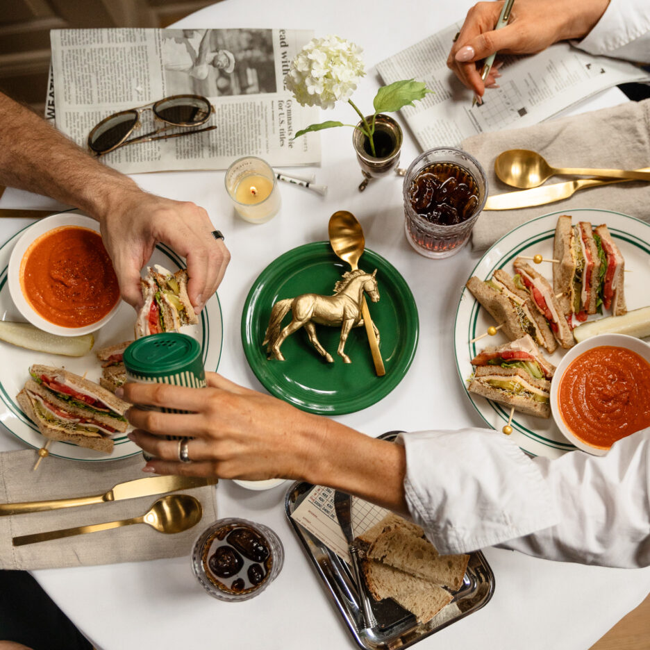 Gold and white dining table with sandwiches, tomato soup, sodas, and a gold horse figurine, elegant table setting, and decorative items, casual lunch or brunch scene.