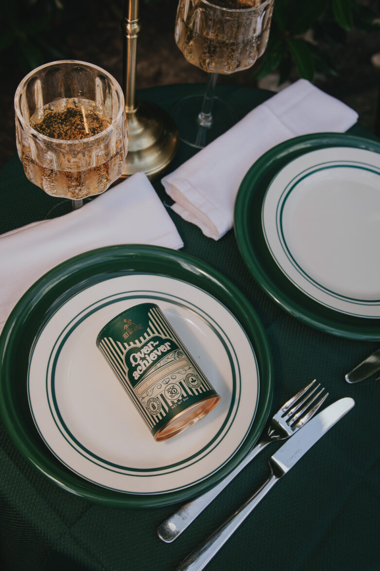 Gold and green tableware with plates, cutlery, and graphic cans, elegant glassware, and white napkins for outdoor dining, stylish and coordinated table setting for special occasions or gatherings.