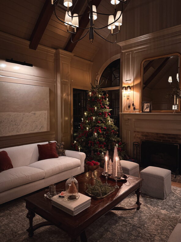 A classic burgundy red bow and candlelit Christmas tree in a moody, modern, traditional living room