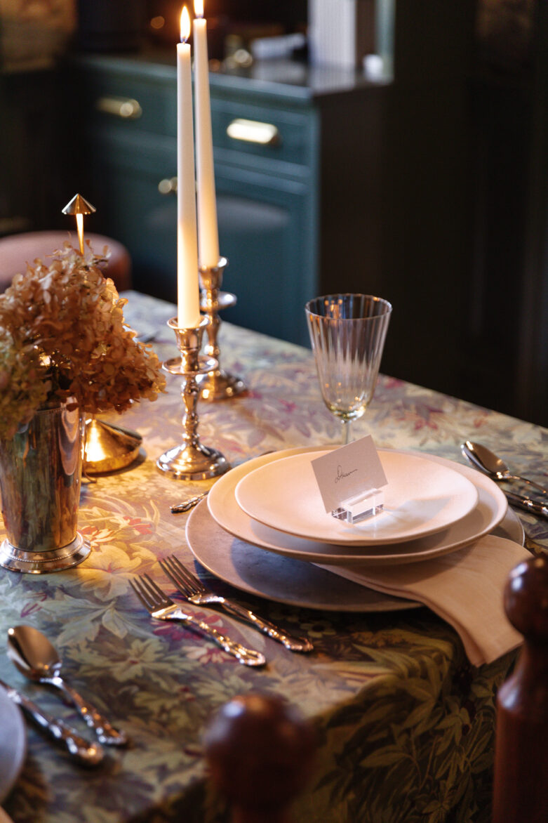 A beautifully set dining table with elegant white dinnerware, crystal glassware, and silverware, illuminated by candlelight, featuring floral arrangements and a cozy, stylish kitchen background, perfect for family gatherings and entertaining.