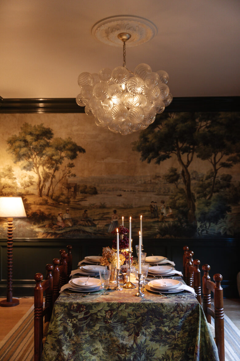 Elegant dining room with vintage chandelier, antique-style wallpaper mural, and a beautifully set table with candles and floral centerpiece, showcasing classic interior design and home decor.