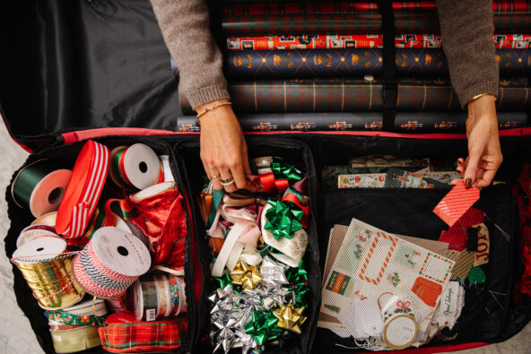 Festive holiday gift wrapping supplies including ribbons, bows, wrapping paper, and holiday-themed decorations organized in a travel case.
