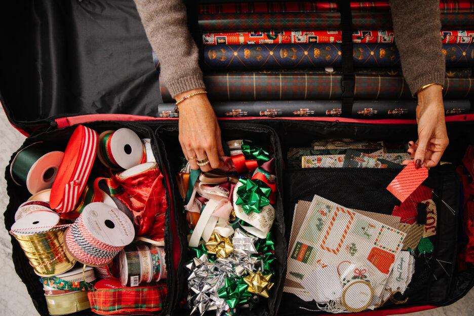 Festive holiday gift wrapping supplies including ribbons, bows, wrapping paper, and holiday-themed decorations organized in a travel case.