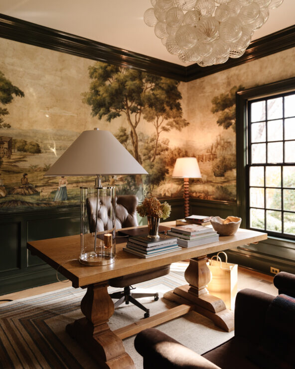 A cozy, sophisticated home office featuring a scenic mural wall, wooden desk with decorative items, tufted leather chair, and natural lighting from the large window. Perfect for inspiring creativity.