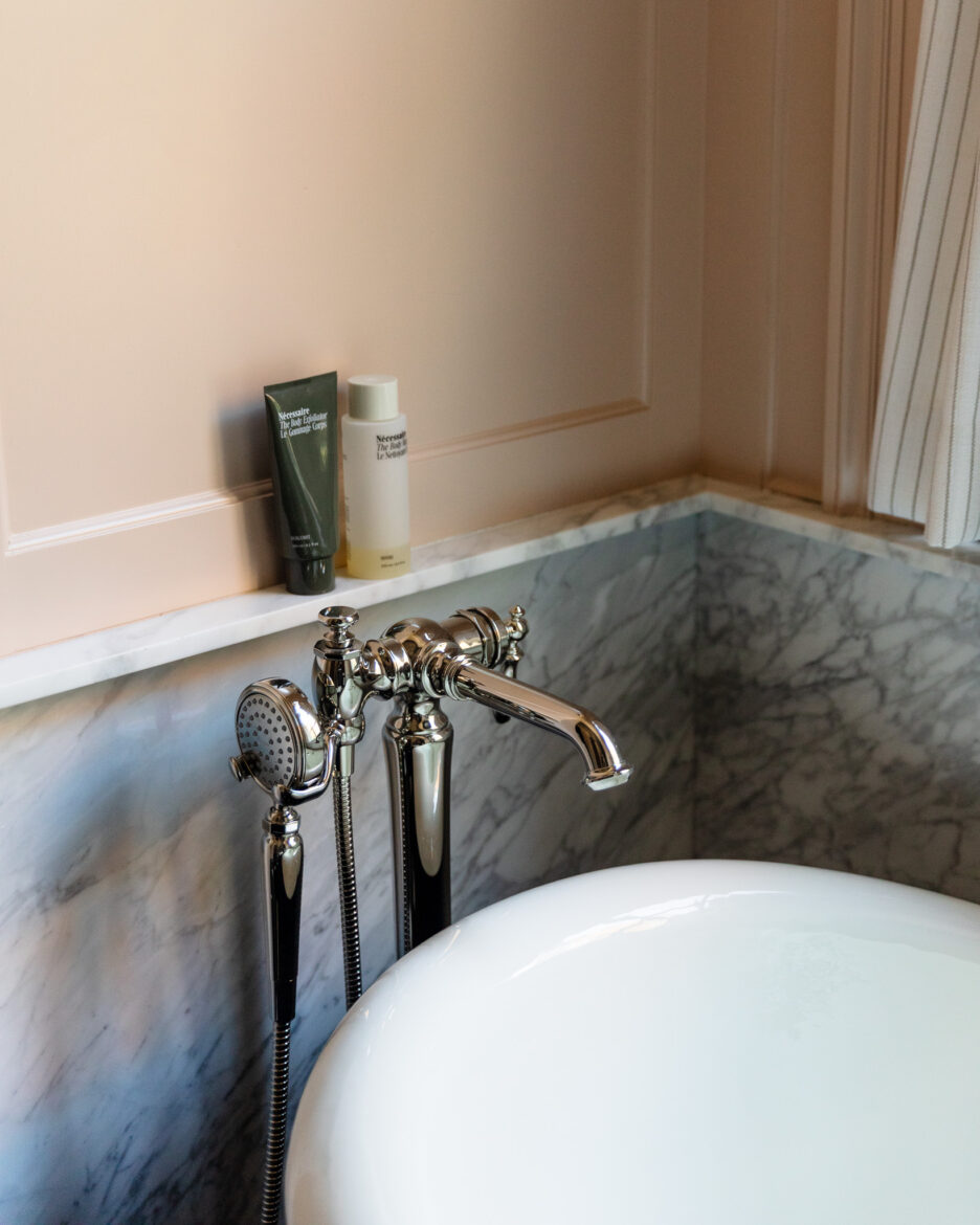 Relaxing bathtub with vintage-style polished nickel fixtures and marble surround, featuring bath salts and skincare products for a luxurious bathroom retreat.