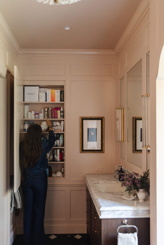 Organizing a bathroom wall cabinet with beauty products, skincare, and toiletries in a luxurious home bathroom.