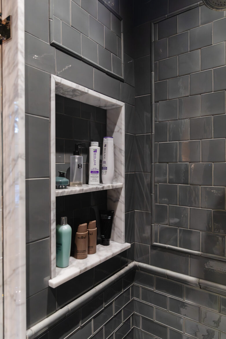 Recessed shower niche with marble border and dark gray subway tiles in a modern bathroom.