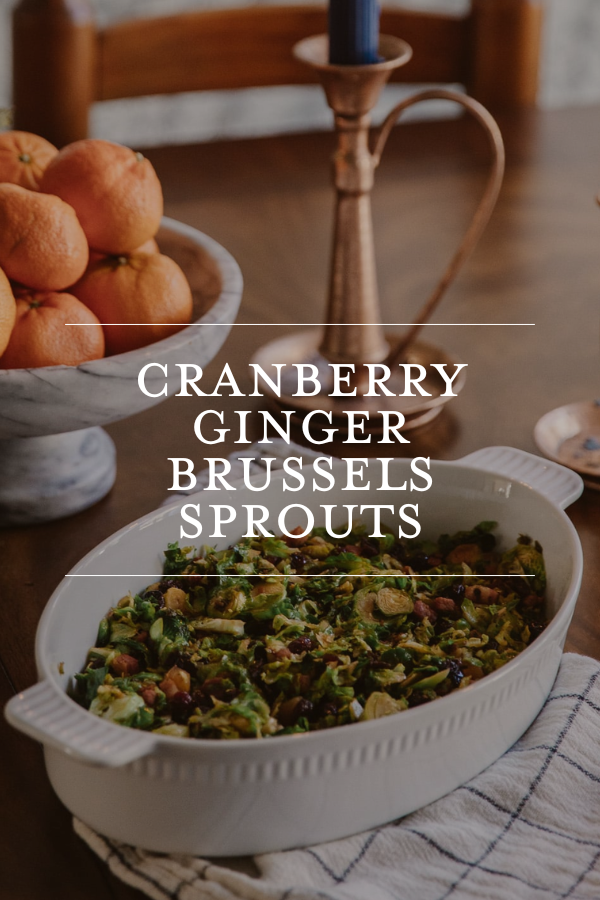 Cranberry ginger Brussels sprouts dish on a rustic dining table with fresh oranges and candle holder, showcasing a cozy, festive meal.