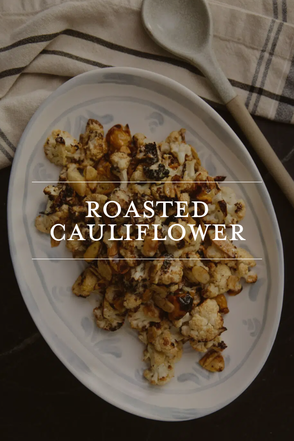 Roasted cauliflower on white serving platter with charred edges, served with a spoon and striped napkin, healthy vegetable dish for dinner or lunch, gourmet roasted cauliflower recipe.