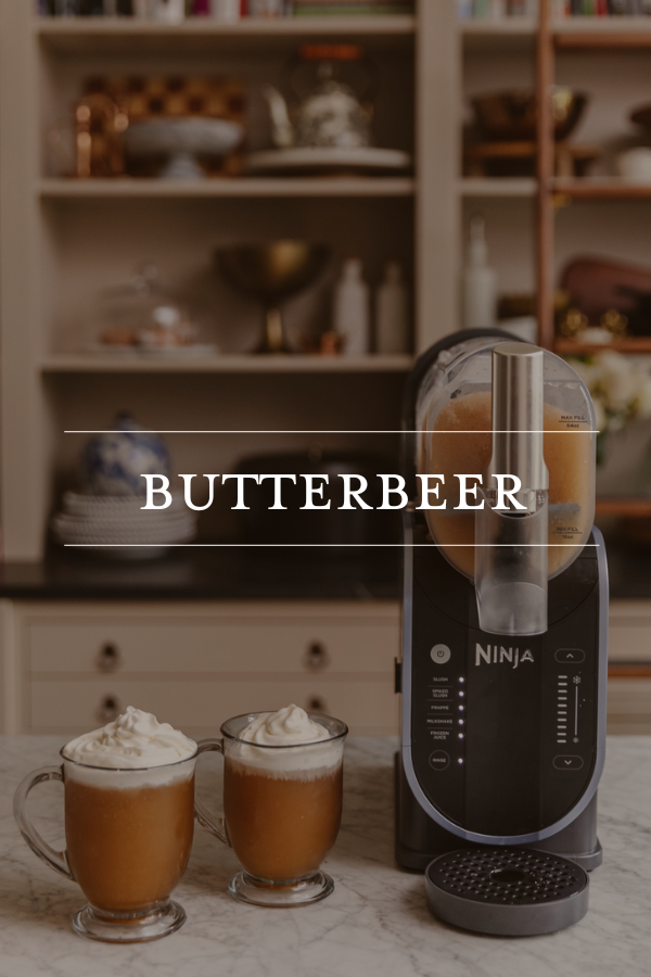Creamy homemade butterbeer with whipped cream served in glass mugs next to Ninja blender, creating a Harry Potter-inspired drink in a stylish, well-organized kitchen setting.