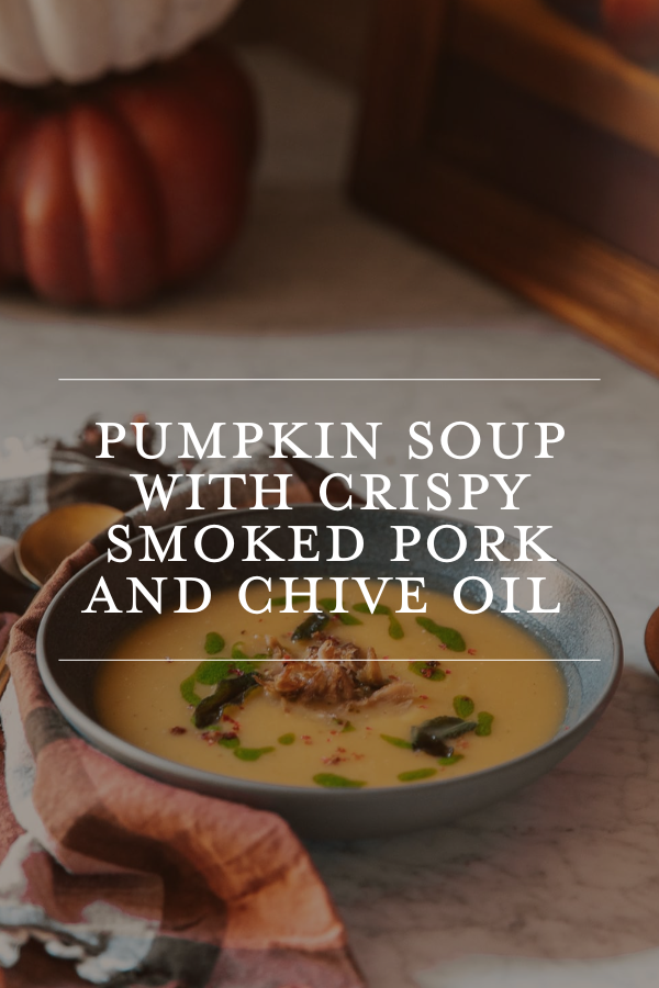Creamy pumpkin soup with crispy smoked pork and chive oil served in a bowl on a kitchen countertop.