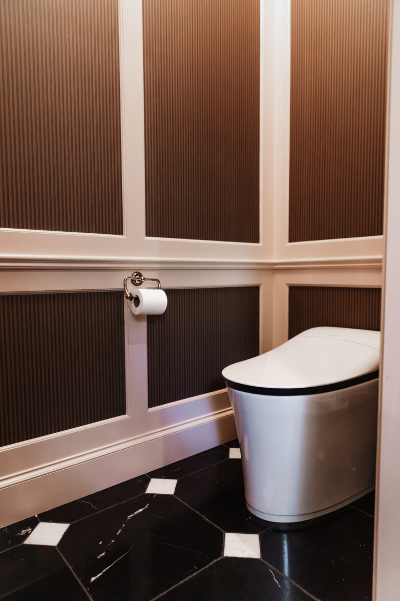 Sleek modern toilet in a stylish bathroom with black and white marble flooring and wood-paneled wainscoting, showcasing contemporary bathroom design and renovation ideas for a luxurious space.