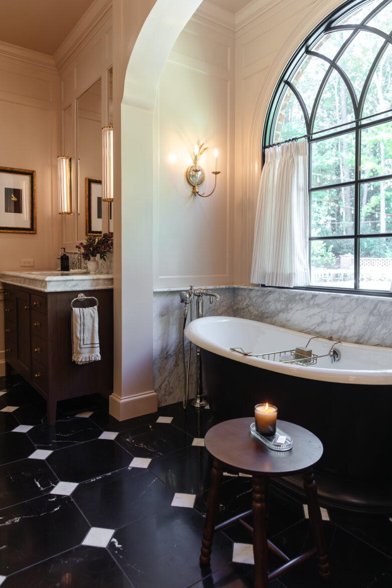 A cozy, elegant bathroom decor showcasing a luxurious black clawfoot tub, large arched window with white curtains, marble backsplash, and warm lighting for relaxing baths.