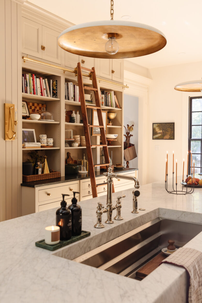 Warm wood-framed glass doors in a modern farmhouse kitchen featuring white beadboard cabinets, open shelving with cookbooks, a wooden ladder, and stylish pendant lighting, blending functionality with cozy aesthetic.