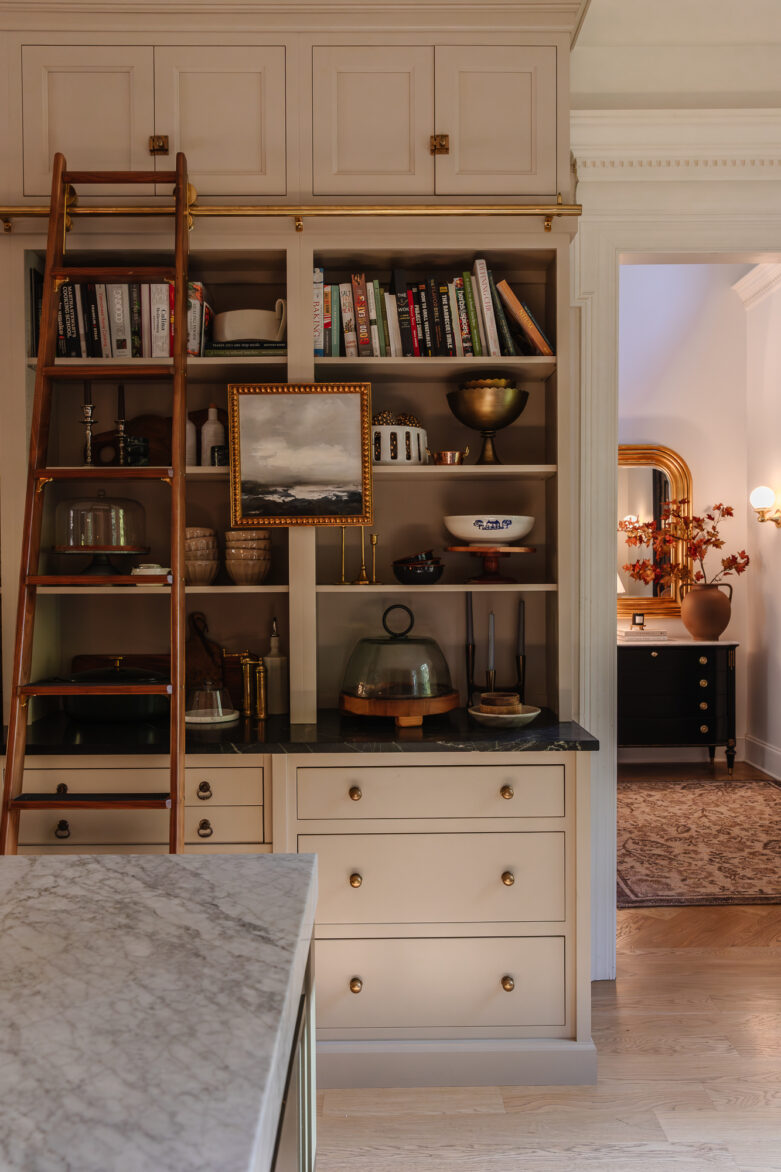Vintage kitchen display with open shelving, decorative dishes, framed artwork, and a ladder for easy access, emphasizing stylish home organization and kitchen aesthetic by Chris Loves Julia.