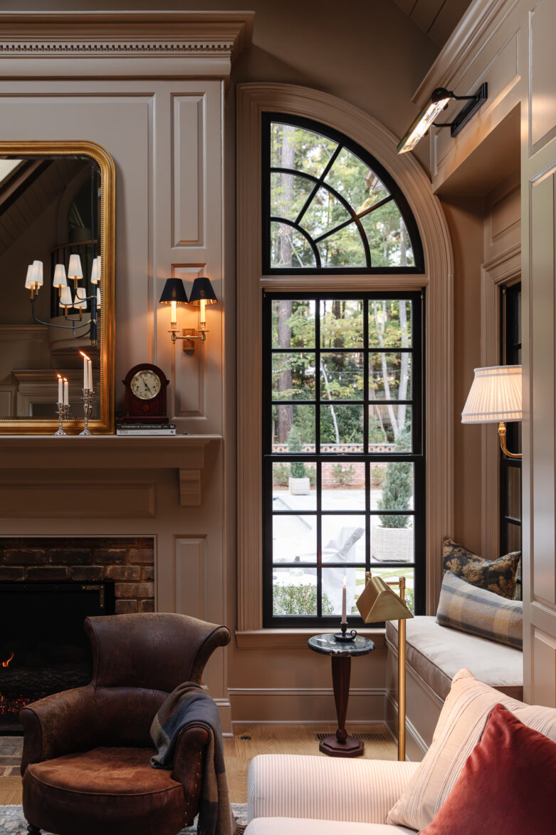 Cozy living room with large arched window, elegant fireplace, and classic decor, showcasing a warm, inviting design with sophisticated lighting and furniture arrangements, from Chris Loves Julia.