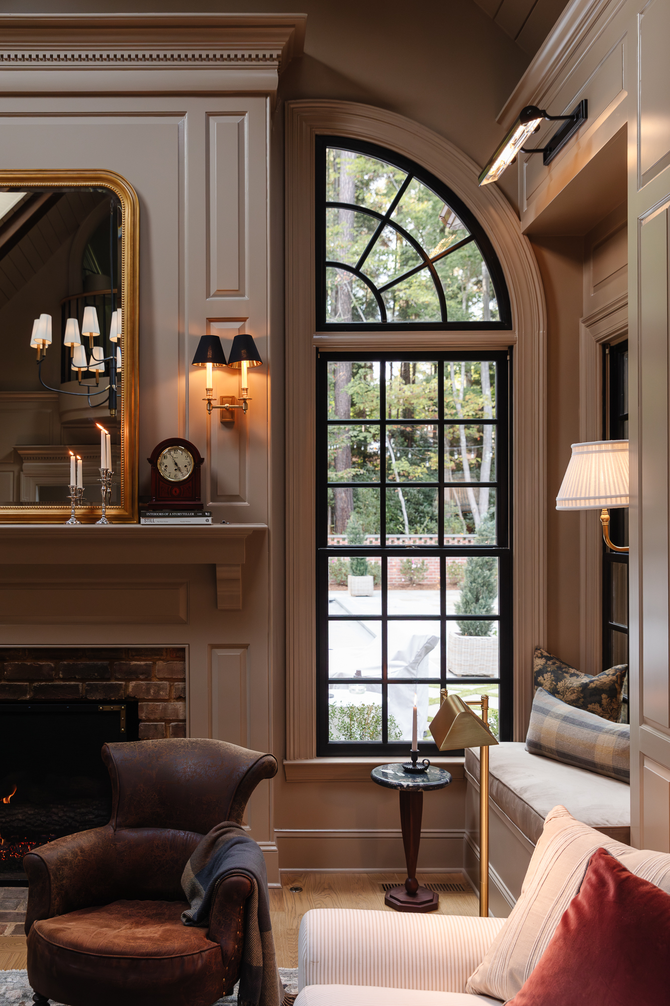 Cozy living room with large arched window, elegant fireplace, and classic decor, showcasing a warm, inviting design with sophisticated lighting and furniture arrangements, from Chris Loves Julia.