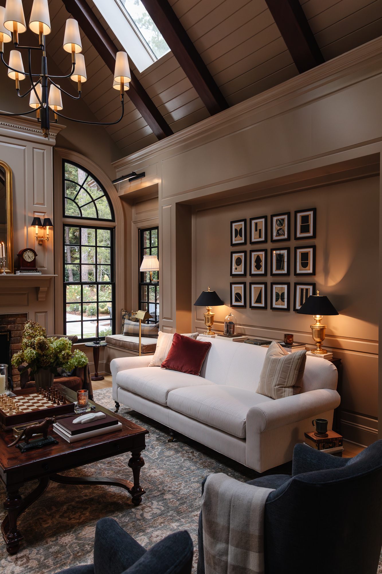 Cozy living room with a high vaulted ceiling, large arched windows, and warm beige walls, featuring elegant decor, a white sofa, and stylish black lamps, showcasing interior design and home renovation inspiration.