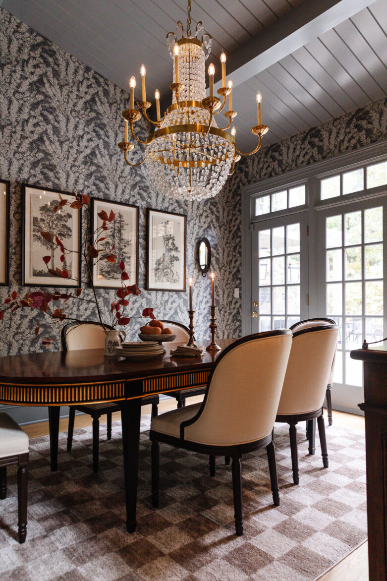Antique chandelier hanging above a vintage-inspired dining room with floral wallpaper, elegant upholstered chairs, and classic decor, creating a sophisticated interior design ambiance.