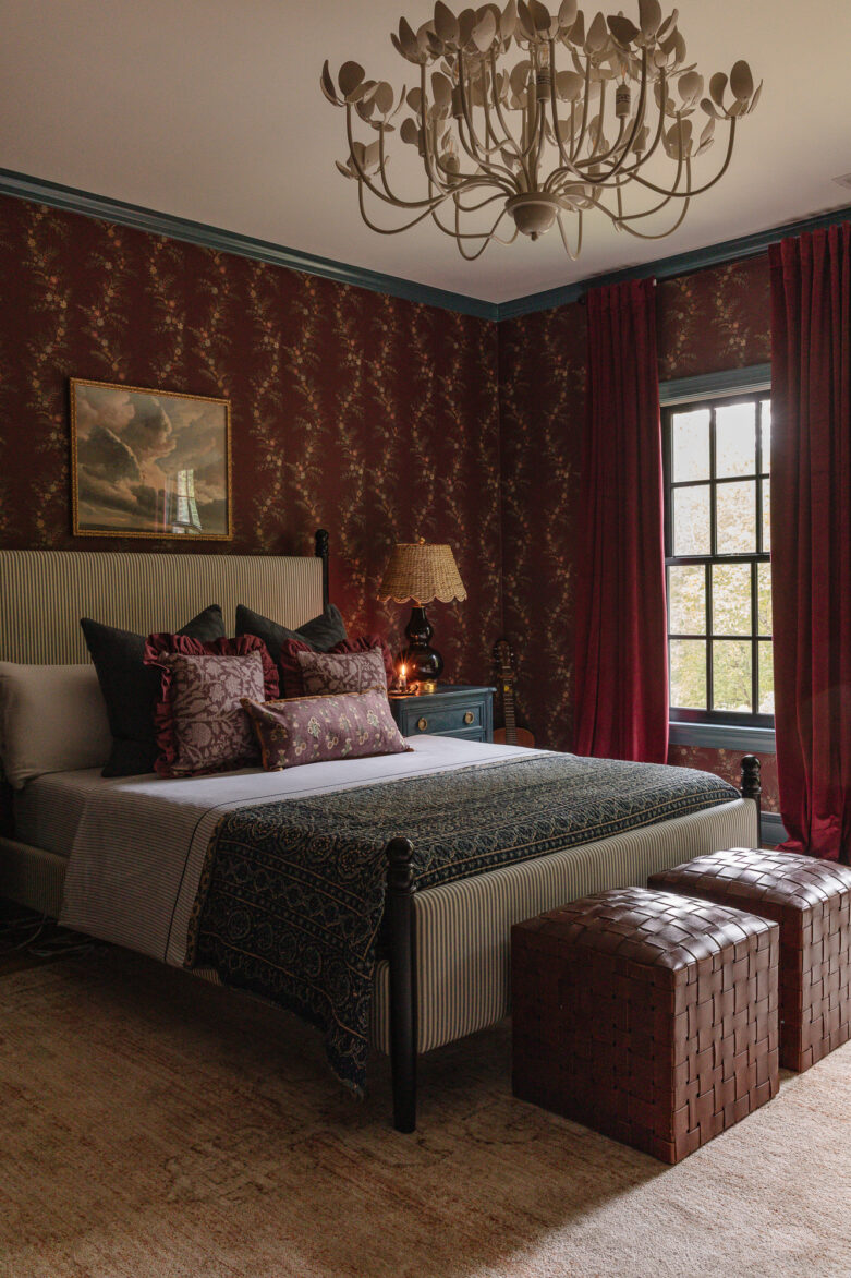 Charming vintage bedroom decor with floral wallpaper, deep red curtains, a striped bed, and cozy pillows creating an inviting and stylish home interior.