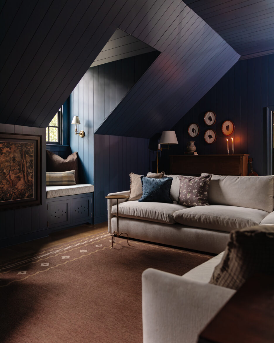 Cozy living room with navy blue paneled walls, sloped ceiling, and vintage-inspired decor, featuring a beige sofa, colorful throw pillows, and warm lighting for inviting home design.