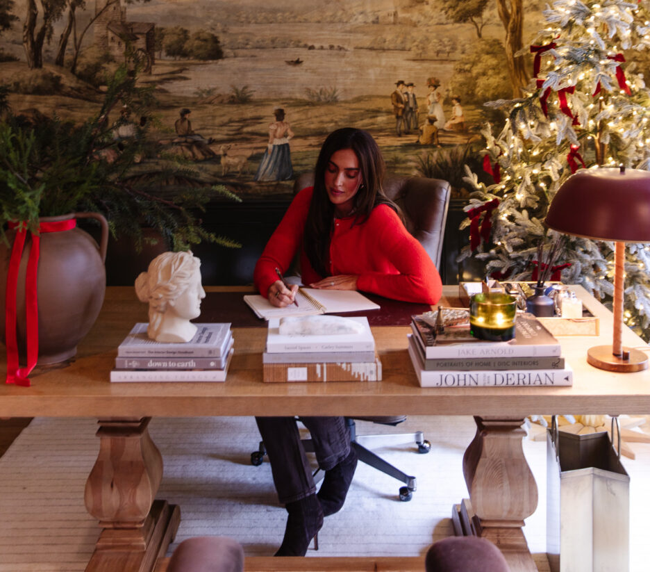 Julia in a red sweater sitting at the desk in the Study writing a card