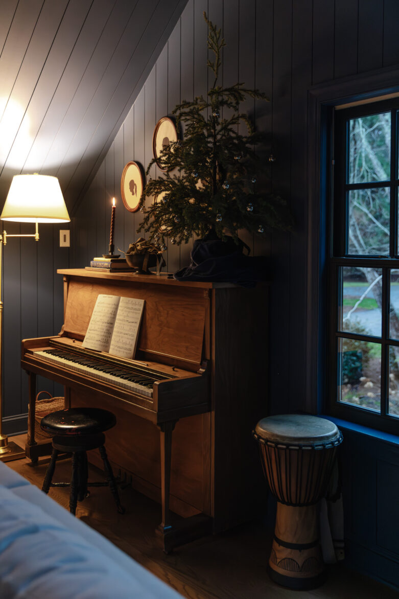 A vintage upright piano with sheet music, a tall potted plant, and warm lighting create a cozy, inviting atmosphere in a beautifully decorated room.