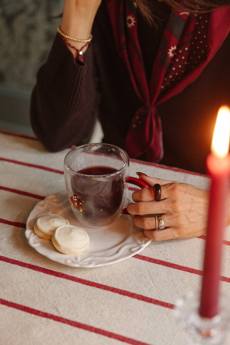 A woman enjoying a warm cup of Glogg with cookies on a festive table.