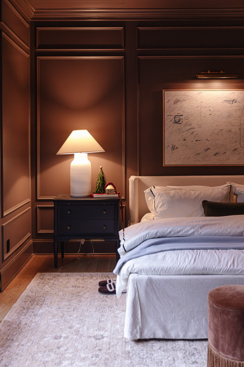 Warm bedroom with dark paneled walls, soft lighting from table lamp, and inviting bedding, showcasing stylish and cozy interior design elements for restful living.