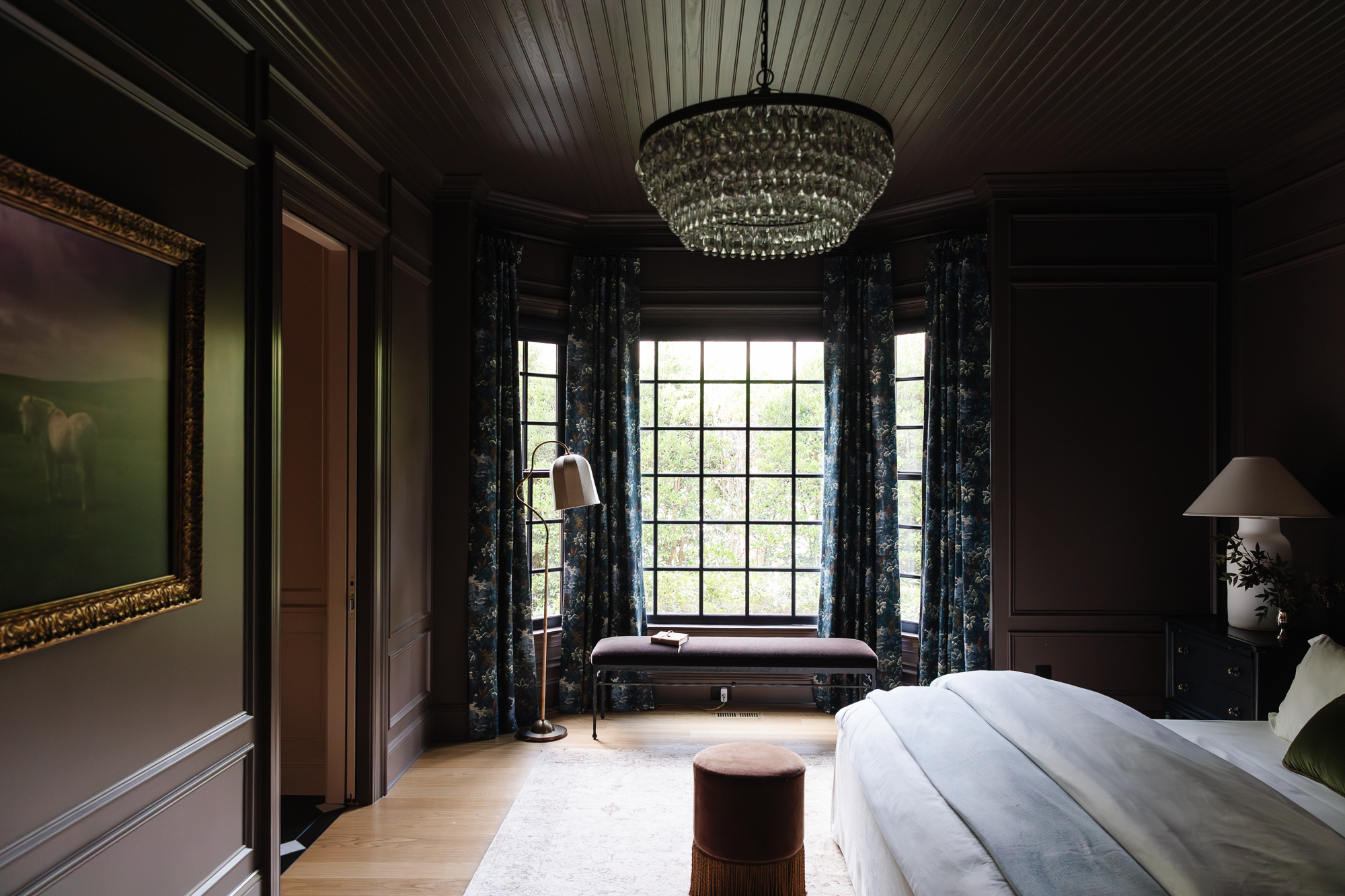 Luxury bedroom interior with dark paneled walls, statement chandelier, floral drapes, and inviting seating area, inspired by Chris Loves Julia home design.