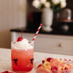 Bright red cherry soda garnished with whipped cream and a maraschino cherry, served with a striped straw; filled with nostalgic candy pasta, perfect for sweet treats and holiday celebrations.