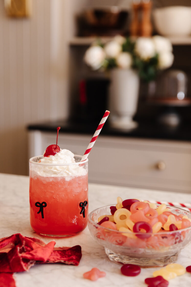 Bright red cherry soda garnished with whipped cream and a maraschino cherry, served with a striped straw; filled with nostalgic candy pasta, perfect for sweet treats and holiday celebrations.
