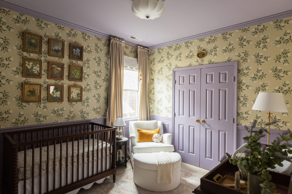 Bright nursery with floral wallpaper, purple accents, and cozy seating area featuring a white armchair and plush toy, creating a calming environment for a baby.