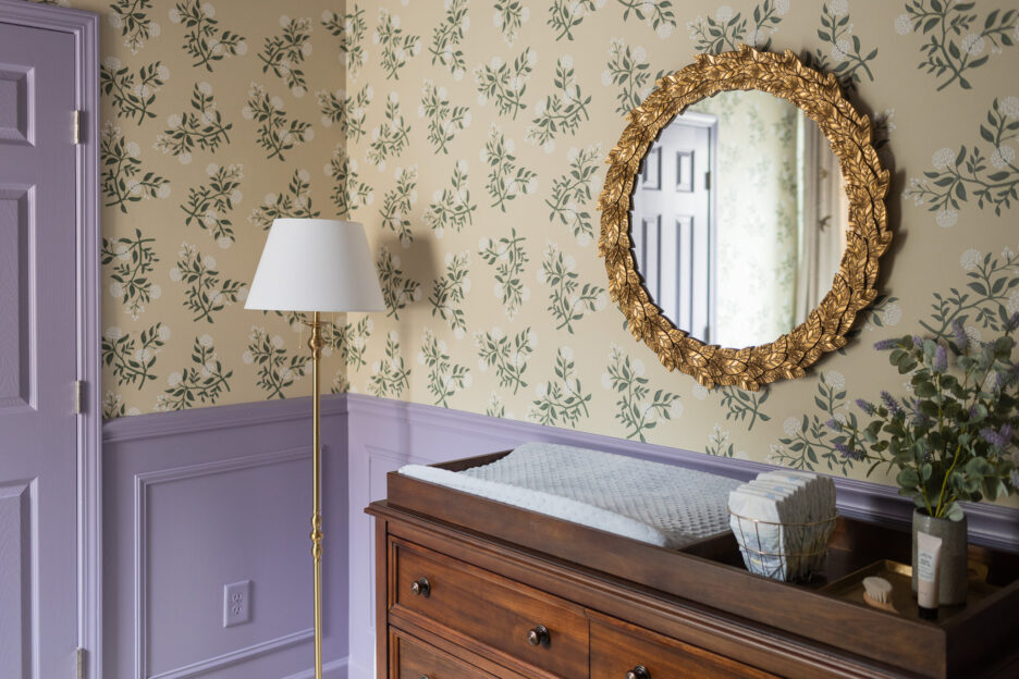 Elegant nursery with floral print wallpaper, gold leaf mirror, and wooden changing table, combining modern and classic styles for a welcoming baby space.